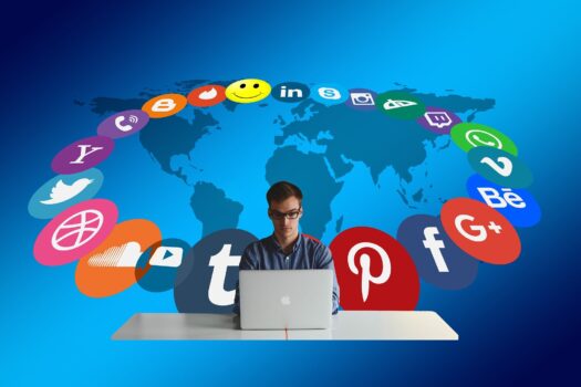 laki-laki di depan laptop deikelilingi logo-logo berbagai channel social media, seperti facebook, path, linked in, instagram dan lain-lain