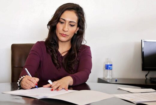 perempuan berpakaian formal sedang menulis di meja kerjanya